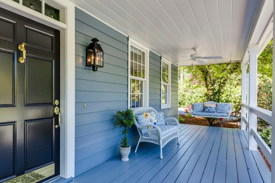 A blue-sided home with a freshly painted porch, white ceiling and black front door