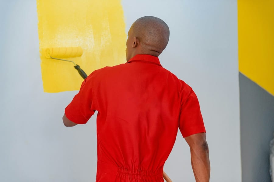A painter rolling bright yellow paint onto an interior wall