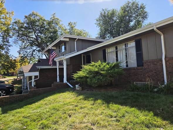 Split-level home with brown siding, white gutters and dark shutters under a clear blue sky
